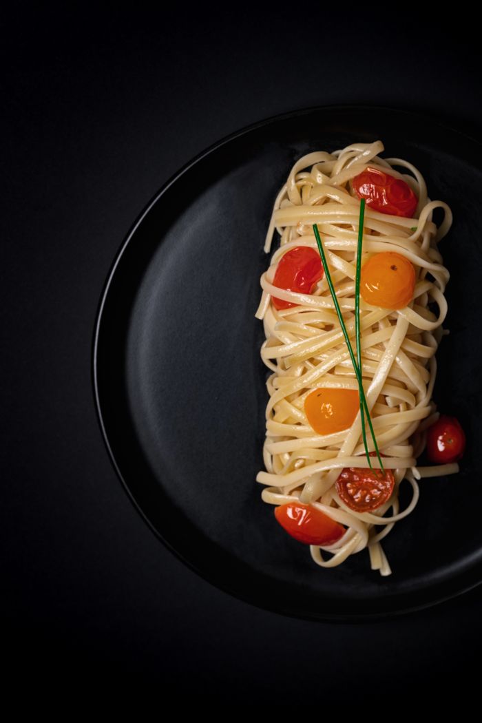 about-bg Delicious linguine pasta with cherry tomatoes elegantly plated on a black dish.