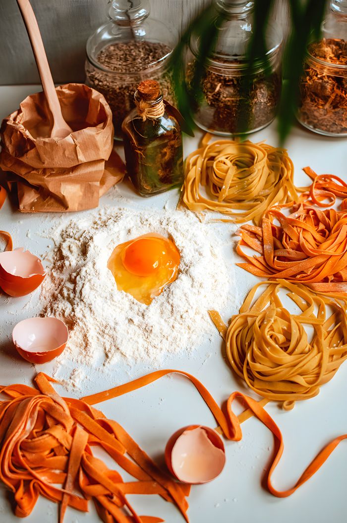 our-story Flat lay of ingredients for making homemade pasta, featuring eggs, flour, and pasta dough.