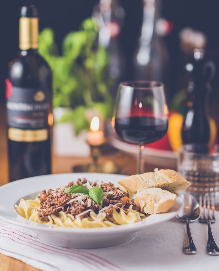 services-03 Delicious pasta meal with red wine, served in a warm restaurant setting.